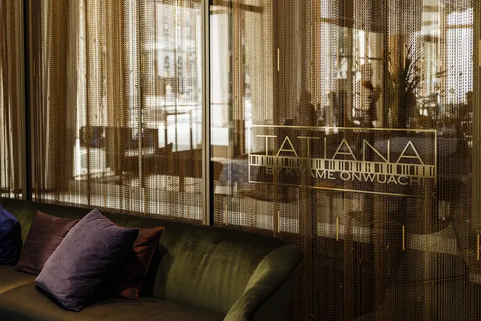 A couch with purple and maroon pillos and a sign above that says "Tatiana."